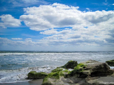 sea with boulders on beach and cloudy blue sky