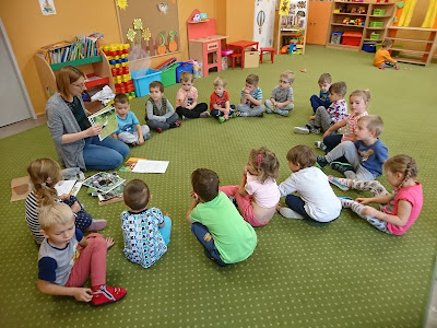 Zdjęcie przedstawia bibliotekarza pokazującego książeczki dzieciom w przedszkolu