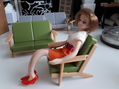 One-twelfth scale modern miniature plastic armchair with a doll sitting in it, in front a similarly-styled sofa
