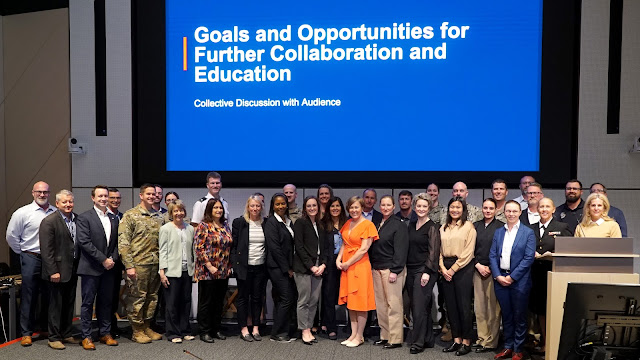 A large group of people pose for a photo in front of a slideshow entitled "Goals and Opportunities for Further Collaboration and Education" at the PES Summit.