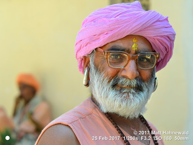 matt hahnewald photography; facing the world; gorakh nath; monk; monastery; bhavnath; bhavnath fair; character; face; earrings; ears; holed; eyes; facial expression; eye contact; full beard; turban; pink; consent; empathy; rapport; respect; traveling; religious; traditional; cultural; hinduism; festival; event; mela; devotee; pilgrim; junagadh; gujarat; asian; indian; western india; one person; male; old; man; senior; picture; photo; face perception; physiognomy; educational; nikon d3100; nikkor af-s 50mm f/1.8g; prime lens; 50mm lens; 4x3 aspect ratio; horizontal orientation; street; portrait; closeup; headshot; seven-eighths view; over-the-shoulder look; outdoors; color; posing; authentic; determined; manly; kanphata; yogi; darshani; gorakhnathi; shaivism; two people; silver; eyeglasses; splitted ears