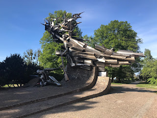 large metal sculpture against a blue sky with trees in the background 