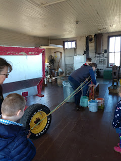 a woman and a small boy hold ends of rope being twisted with a large metal wheel