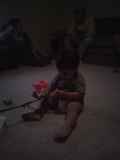 Picture of the baby with his toys surrounding him, he is holding the handle section of Bob's leash.