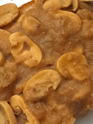 Close up photo of golden brown gravy full of sliced mushrooms on a slice of gluten-free bread.