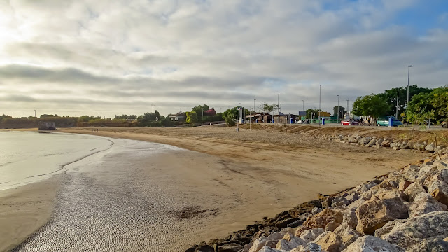 Playa llana de arena bacia con el cielo con muchas nubes.