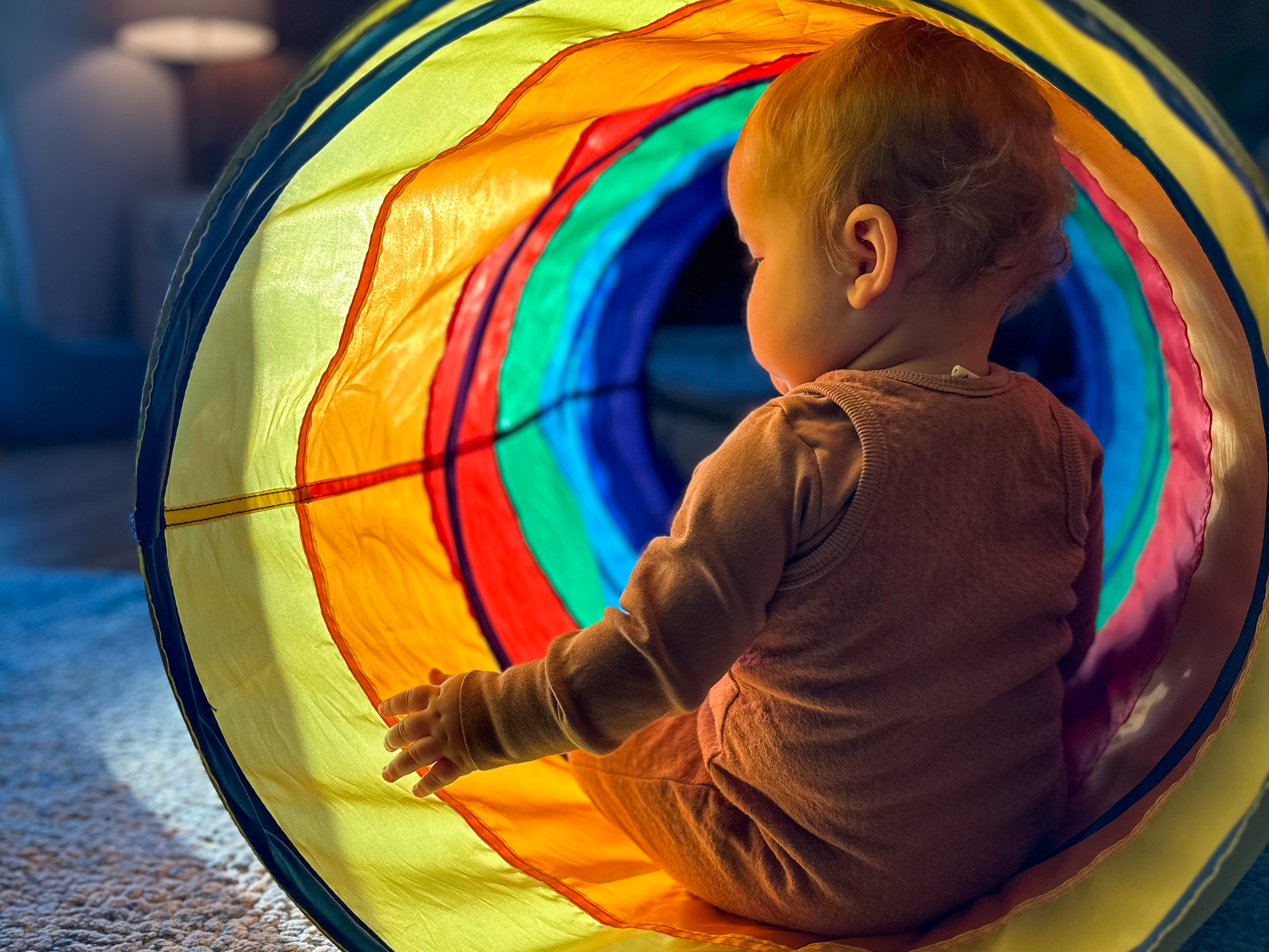 Baby sits backwards in sunny play tunnel in her Montessori home