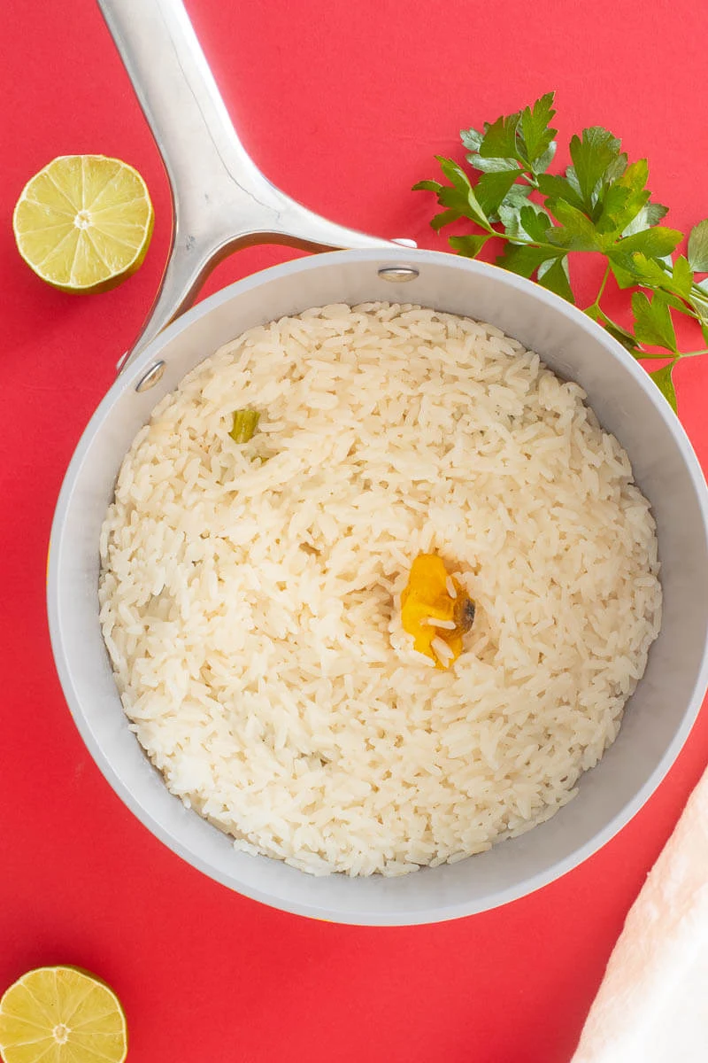 Steamed coconut rice in a pot on a red counter top with the pepper on the inside.
