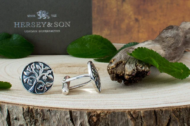 Close up of silver cufflink father's day gift idea with a tree etched on them from Hersey & Son on some wood with leaves