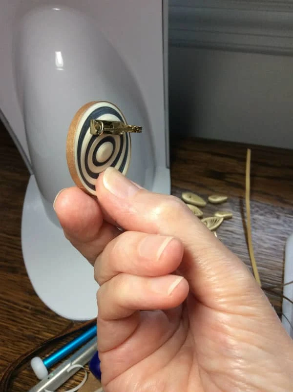 fingers holding reverse side of circular, striped brooch under light