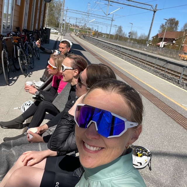 Syklister sittende på rekke på en togstasjon med kaffe og kanelboller