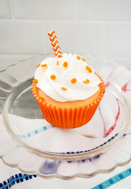 Orange Creamsicle Cupcake on a glass plate with white napkin underneath.