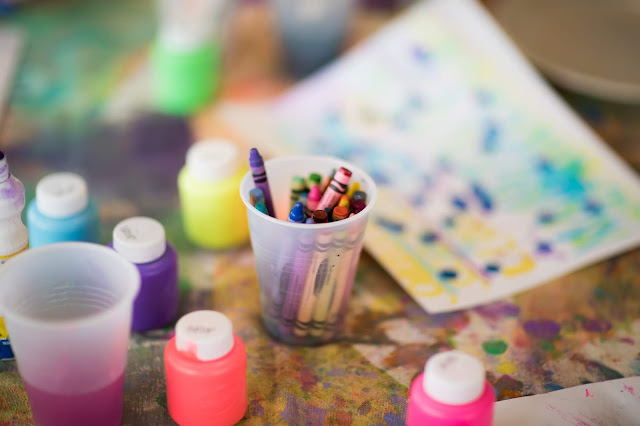 Table showing a pot of paints, crayons and paintings 