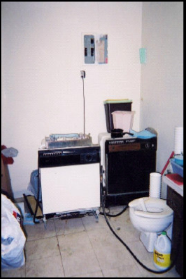 A small, cluttered room with a toilet near a portable dishwasher