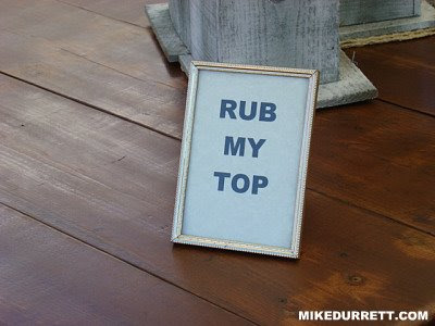 Framed sign says: RUB MY TOP