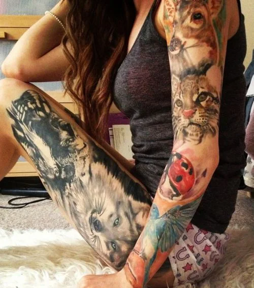 chica sentada , lleva pijama corto, y esta tatuada con animales por todo el cuerpo, tatuajes de lobos, tatuajes de gatos, tatuajes de ciervos