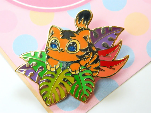 A pin badge of a cute tiger cub sitting in a bunch of colourful leaves