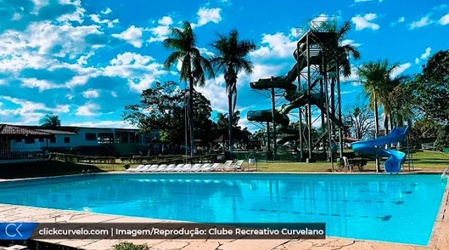 Foto do Clube Recreativo Curvelano, Piscina em primeiro plano e escorregador em espiral ao fundo. Cadeiras em fileira em segundo plano.