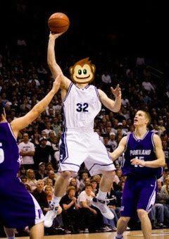 Action photo of a basketball player going up for a jump shot. He has the head of the Greasemonkey logo (a smiling monkey)