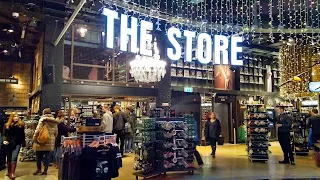 Large white sign in lights saying "The Store" hangs from the ceiling with additional cristmas lights hanging down. Below the sign are many shelves of merchandise and people shoppign