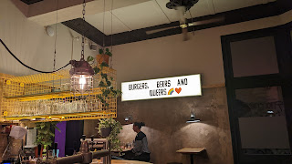 A bar with suspended metal shelving and a neon sign which says Burgers, Beers and Queers