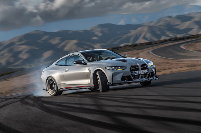 2023 BMW M4 CSL - drifting on a left hand corner so that the in this front view picture the left side of the car is shown; rear wheels are willing to overtake the front wheels as it's usually in controlled drifting; smoke from the rear wheels.