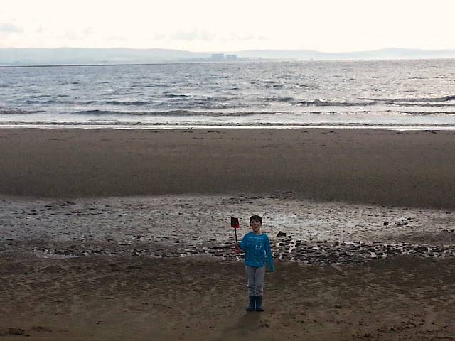 Boy standing on large beach, holding spade. 