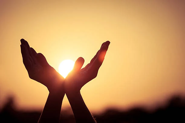Person holding a prayer card with sunrise in background, symbolizing inspirational religious messages.