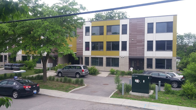 Mid-rise Apartment complex in central Ottawa. Tree and sparsely occupied parking lot in foreground.