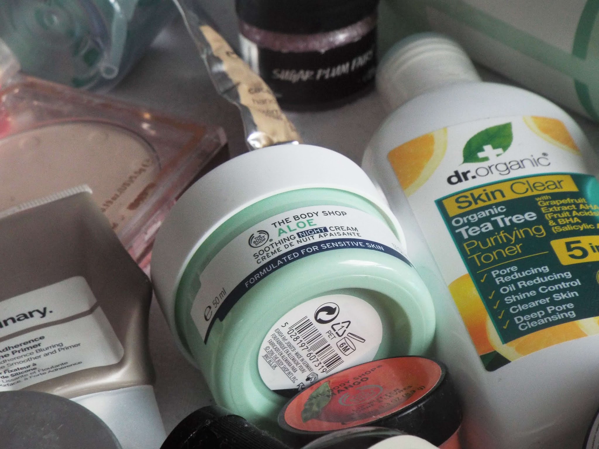 The Body Shop Aloe Soothing Night Cream, mingled amongst other productsin the flatlay, in pale green screw top pot.