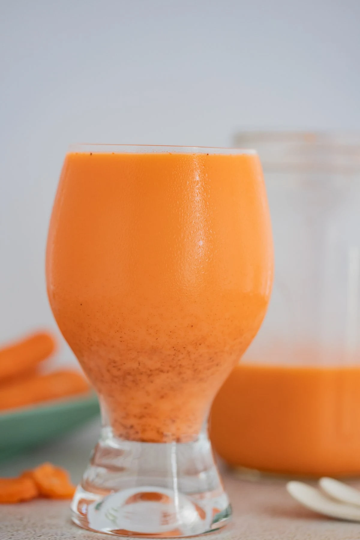 A straight on picture of a glass filled with Caribbean carrot juice with the spices dropping down.