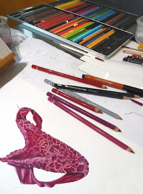 Table de l'atelier avec le dessin en cours de réalisation entouré de crayons divers.