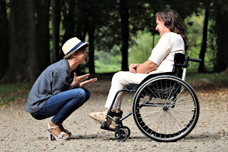 Young adult talking to woman seated on black folding wheelchair