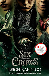 Book cover for the Six of Crows Netflix tie-in edition, featuring Inej, Kaz, and Jesper in a dark green theme