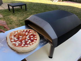Putting pizza into the outdoor Ooni Koda pizza oven