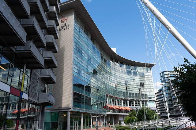 large glass fronted building with cables and tower of suspension bridge to right