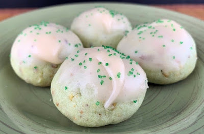 Round pistachio cookies topped with browned butter icing and green sprinkles, photographed on a green plate.