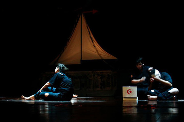 Two young actors sitting on a stage with very little light in an object that appears to be a boat