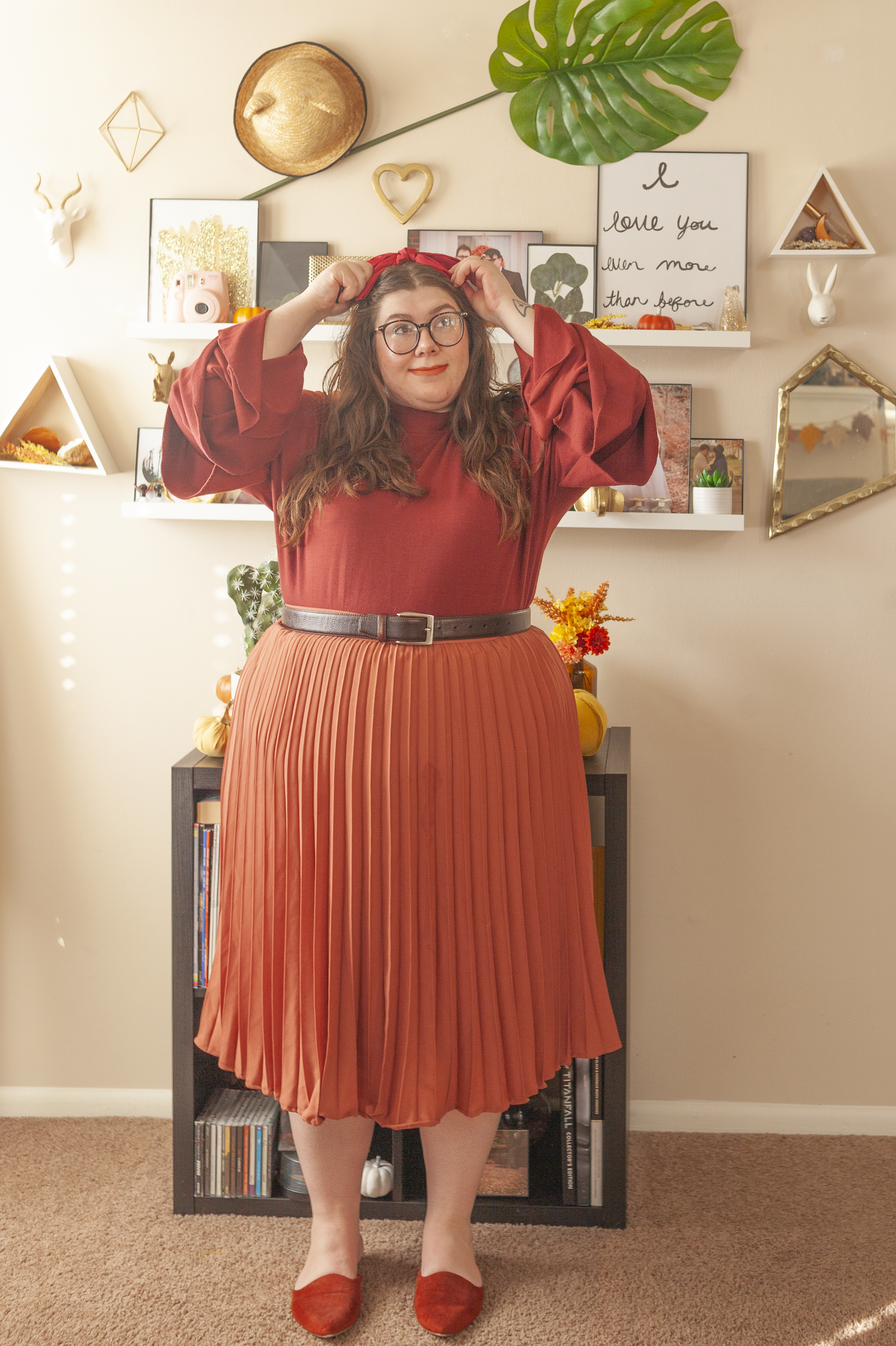 An outfit consisting of a rust red brown long sleeve blouse with tears tucked into a rose colored pleated midi skirt and burnt orange mules.