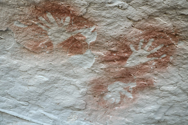 Red silhouette handprints on white sandstone