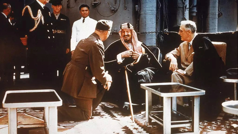 O presidente americano Franklin Delano Roosevelt (à esquerda, 1882-1945) se encontra com o Rei Ibn Saud (à direita, 1880-1953) da Arábia Saudita, chefe de gabinete William D. Leahy (ajoelhado, 1875-1959) e o Coronel William A. Eddy (à direita de Leahy, 1896-1962), ministro para a Arábia Saudita, a bordo de um navio de guerra dos EUA, em 20 de fevereiro de 1945 | Arquivos: Hulton Archive/Getty Images