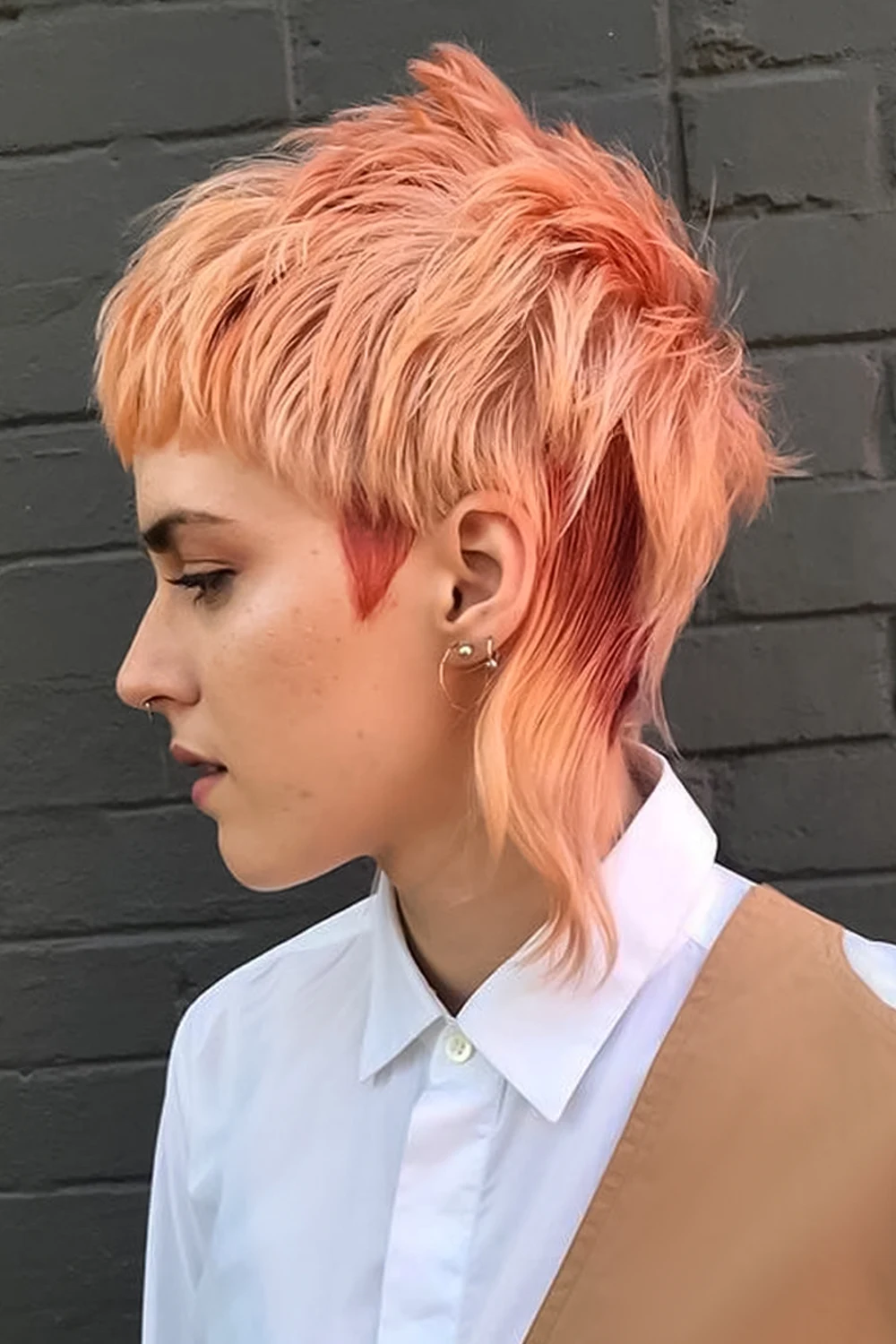 woman with dyed edgy mullet haircut is posing on brick background