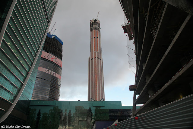 Construction photo of front slim side of the Mercury City Tower along with the other skyscrapers under construction