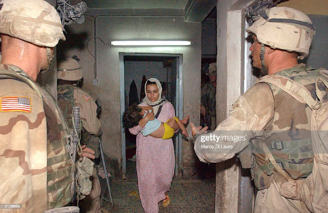 An Iraqi mother leaving her apartment as US soldiers inspect for suspects