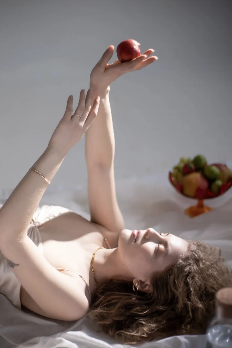 beautiful young woman with curly hair is laying on thr floor and holding an apple in her hand