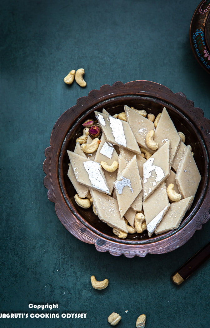 Kaju katli arranged in a bowl with some cashews and dried rose petals on the side