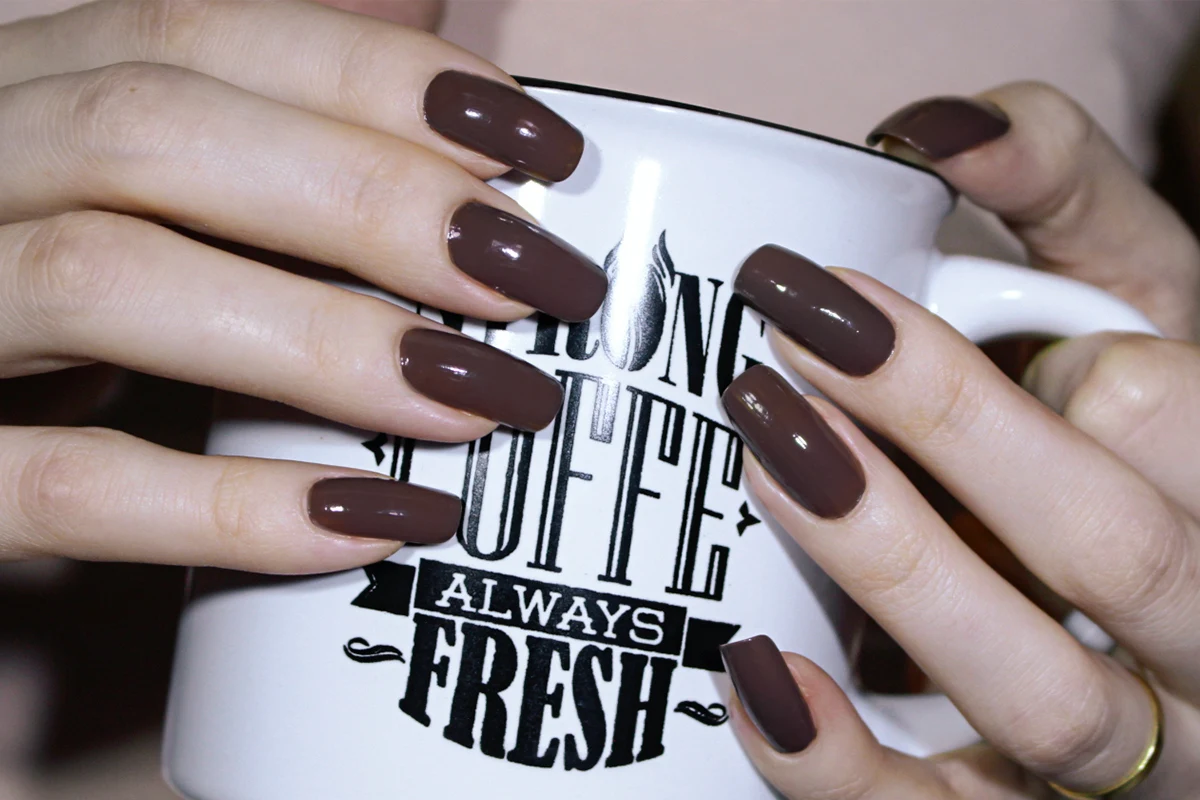 a close-up of woman's hands holding a mug with a pretty brown manicure and long natural nails