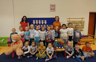 Zdjcie grupowe. Grypa przedszkolaków z panią przedszkolanką i bibliotekarką. Tło: sala przedszkolna.