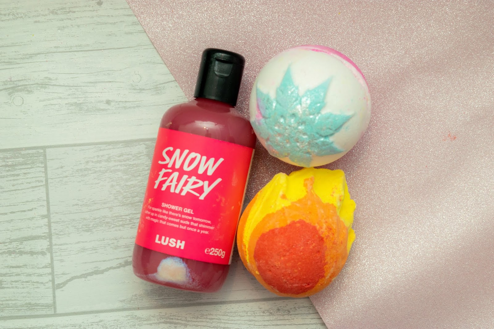 A pink shower gel and two bath bombs. One is white with a blue snowflake and the other is shaped like a fireball.