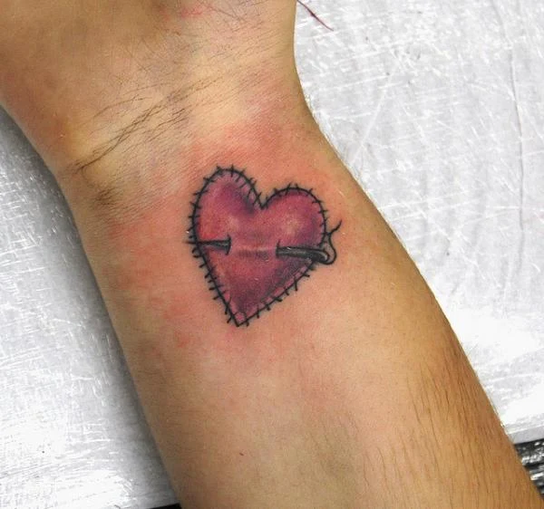 tatuaje en la muñeca de una chica de un corazón cosido de estilo infantil la aguja atraviesa el corazon tatuado